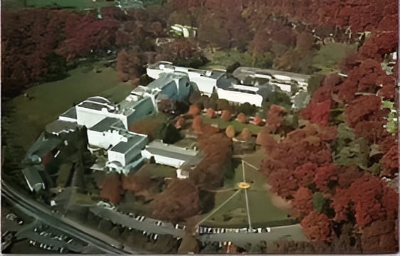 Aerial view of a low-rise complex surrounded by autumn trees and parking areas.