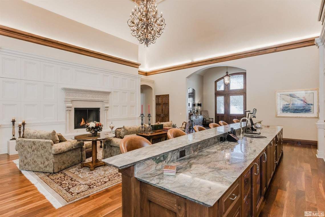 Furnished kitchen and living room with a marble island, paneled fireplace wall, and chandelier.