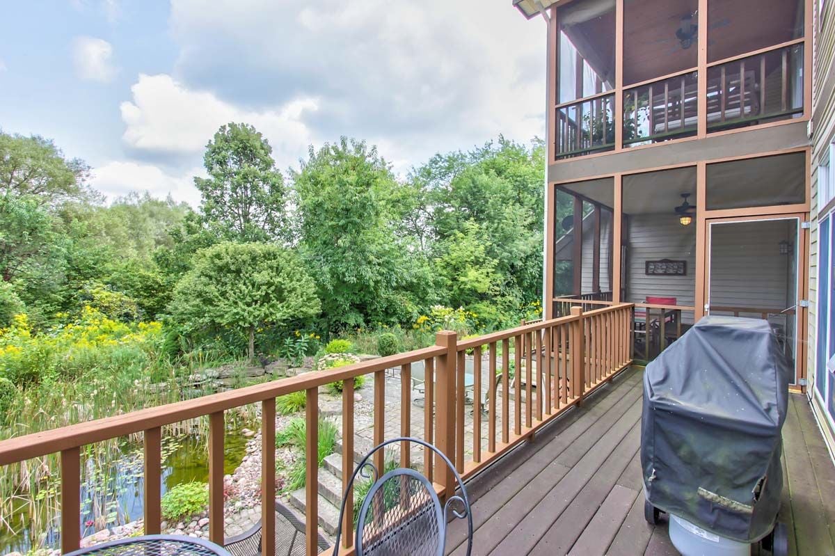 Wooden deck and screened porch overlook a lush garden pond; a covered grill and metal chairs sit on the deck.