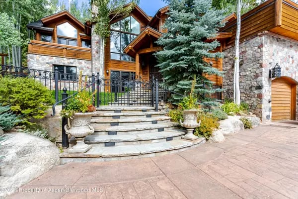 Aspen home with timber and stone exterior, curved stone steps, and mature trees.