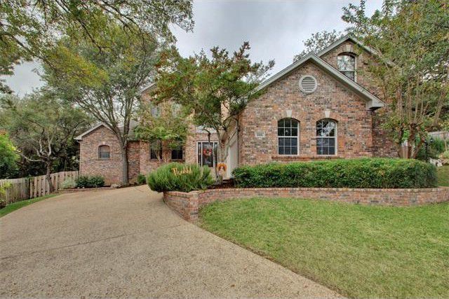 Brick home with a curved driveway, landscaped lawn, and mature trees.