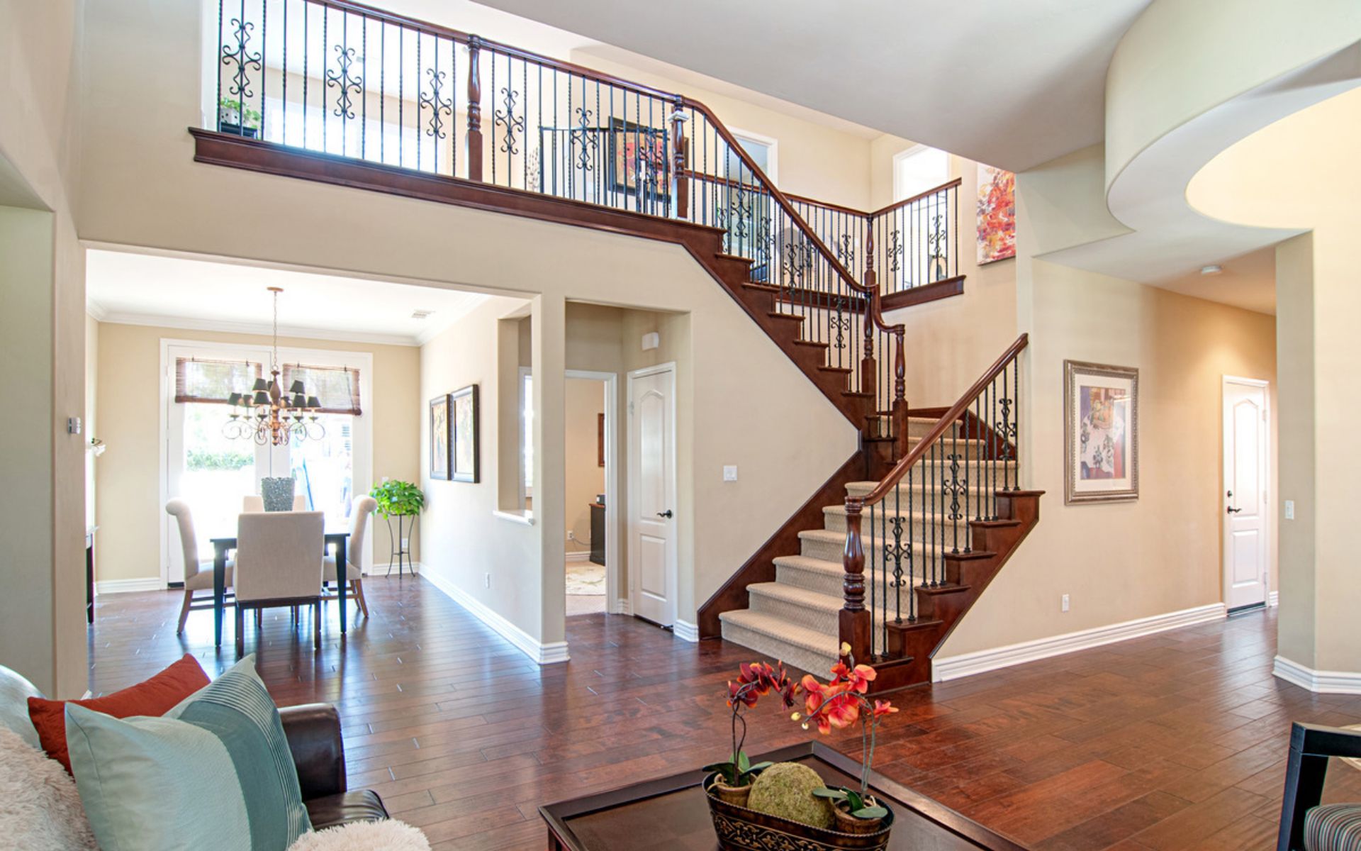 Two-story foyer with a sweeping wood staircase, iron railings, hardwood floors, and an adjoining dining area.