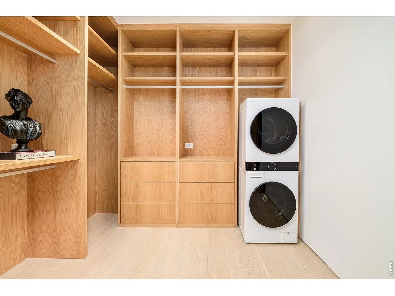 Laundry room with light wood built-ins, open shelving and a stacked washer and dryer.