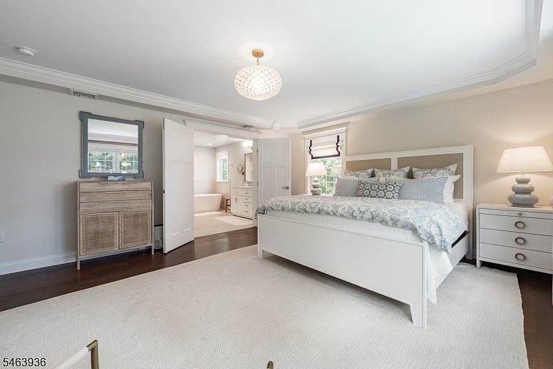 Bright bedroom with a white bed, patterned bedding, and an open doorway to an ensuite bathroom.