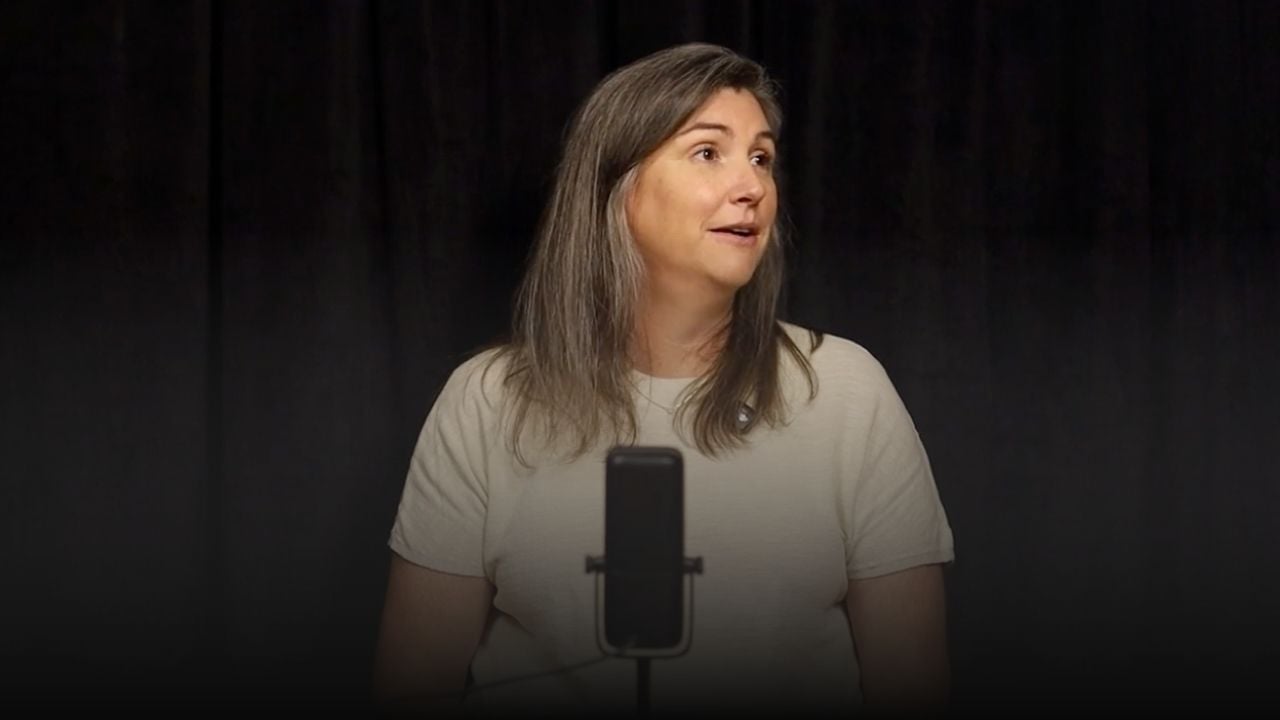 Woman speaking into a microphone against a black curtain.