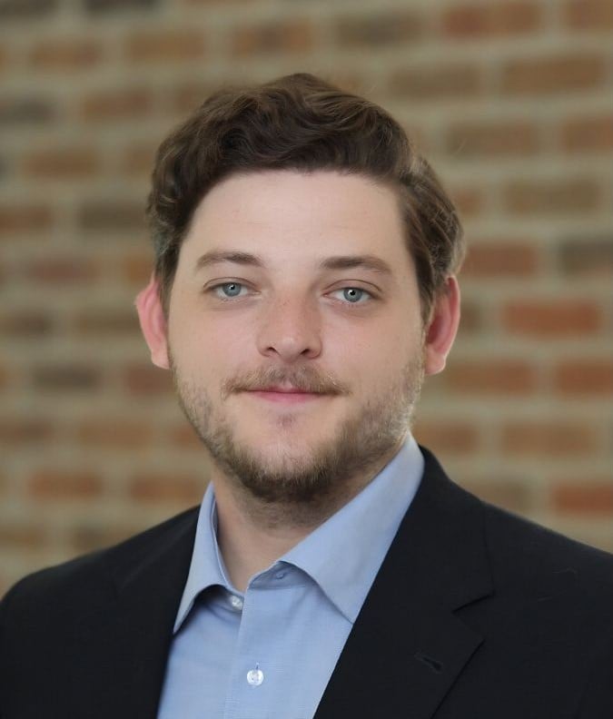 Ben Lazarus in a dark blazer and light blue shirt against a brick wall.