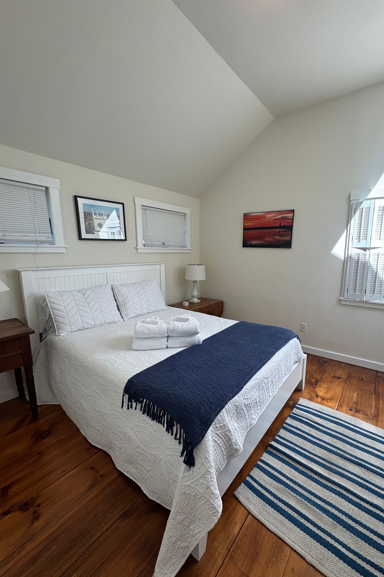Bright bedroom with a white quilted bed, folded towels, and navy throw beneath a vaulted ceiling.
