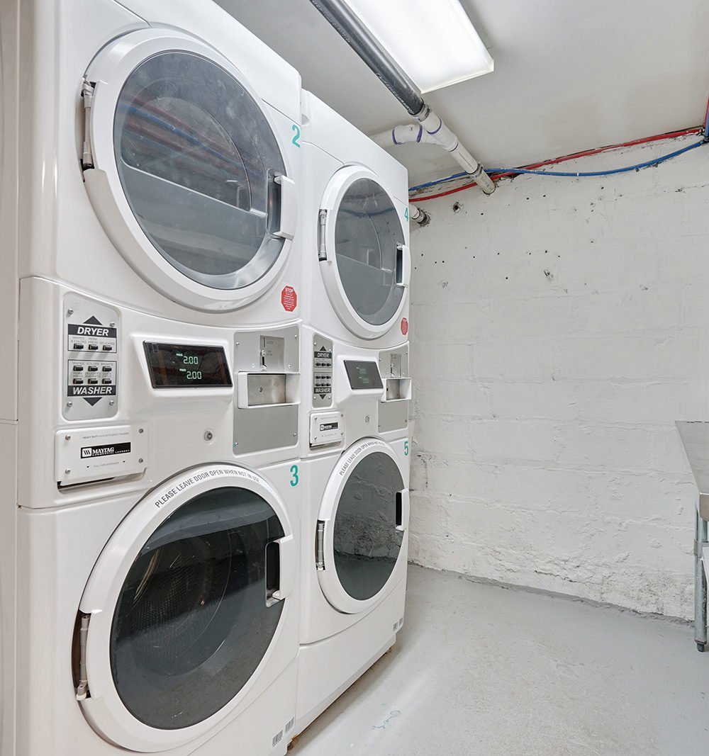 Laundry room with four white commercial Maytag washer-dryer units against a painted masonry wall.