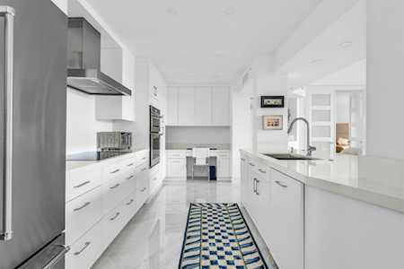 Modern white kitchen with a central island, stainless-steel appliances, and a patterned runner rug.