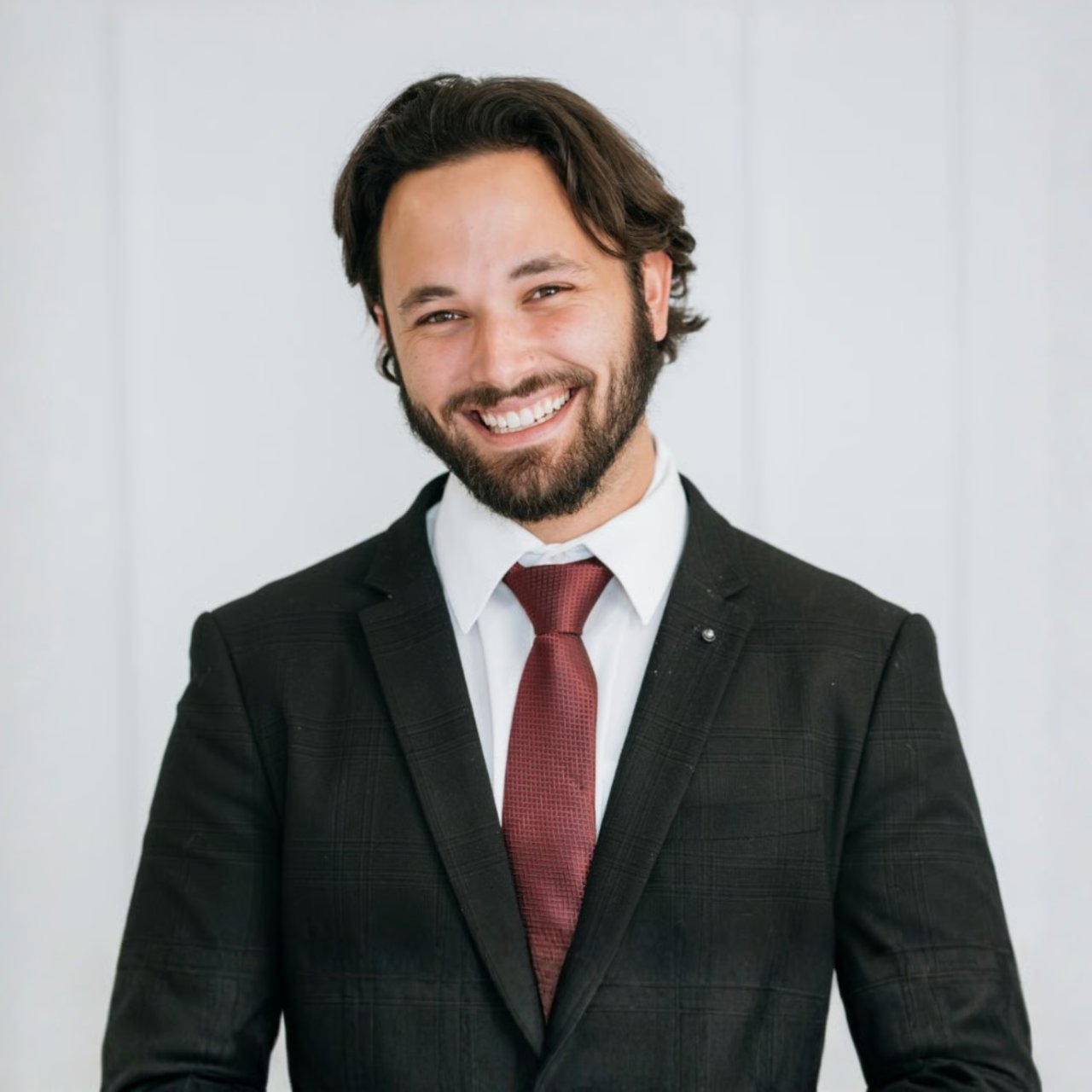 Smiling bearded man in a dark suit and burgundy tie.