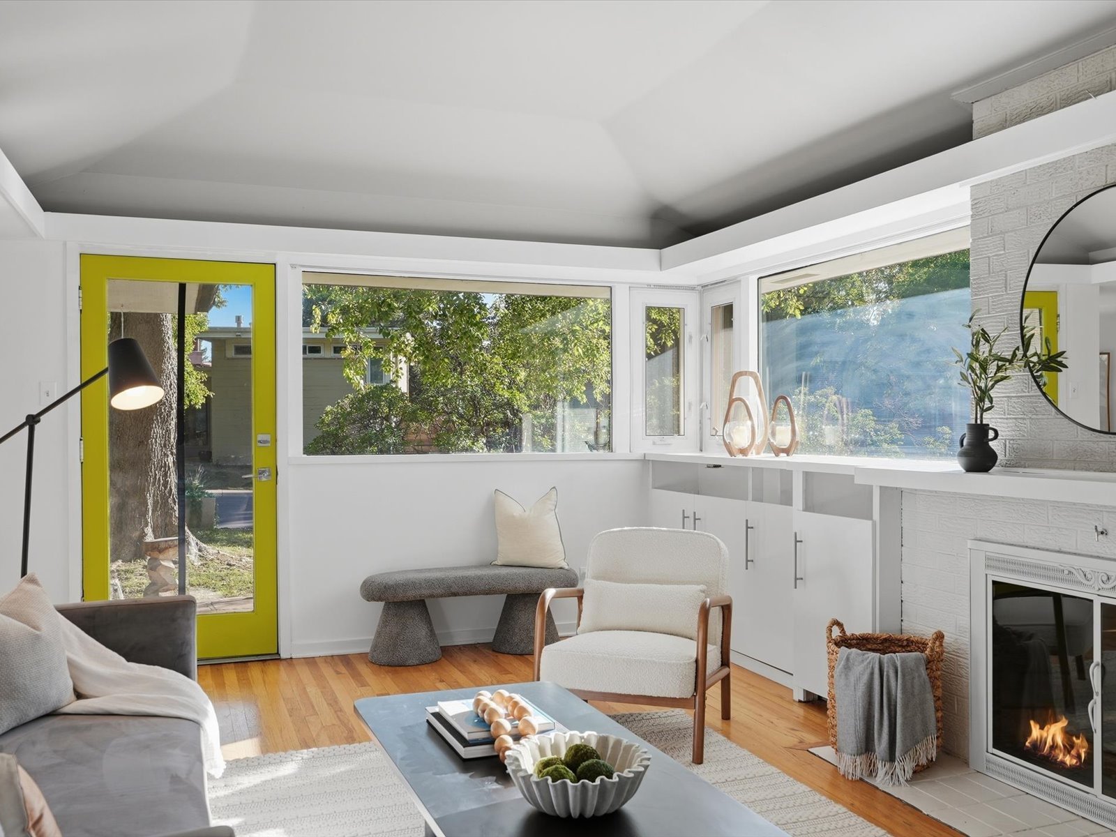 Living room with a bright yellow door, broad garden-facing windows, and a white brick fireplace.