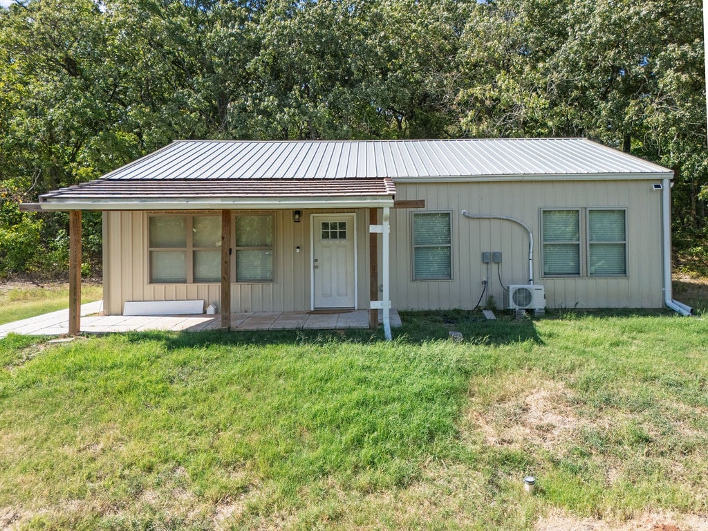 Single-story home with a metal roof and covered porch, surrounded by trees.