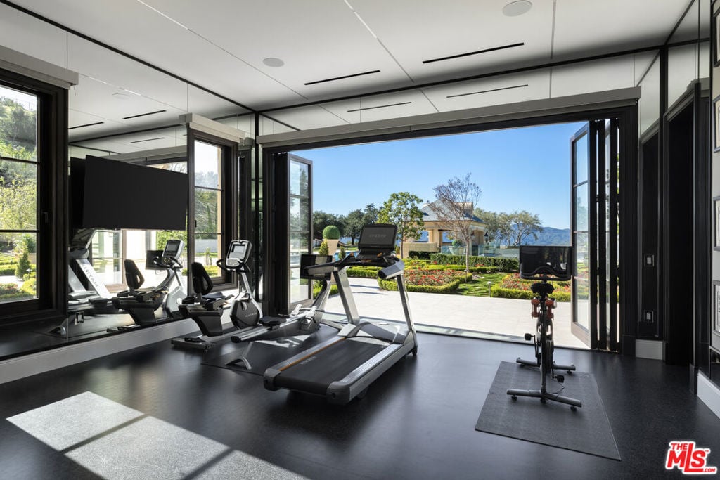 Modern home gym with cardio equipment and open doors overlooking a landscaped garden.