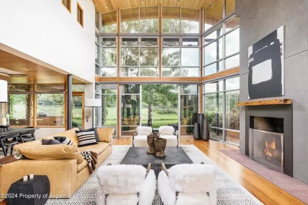 Double-height living room with floor-to-ceiling windows, a stone fireplace, and views of green grounds.