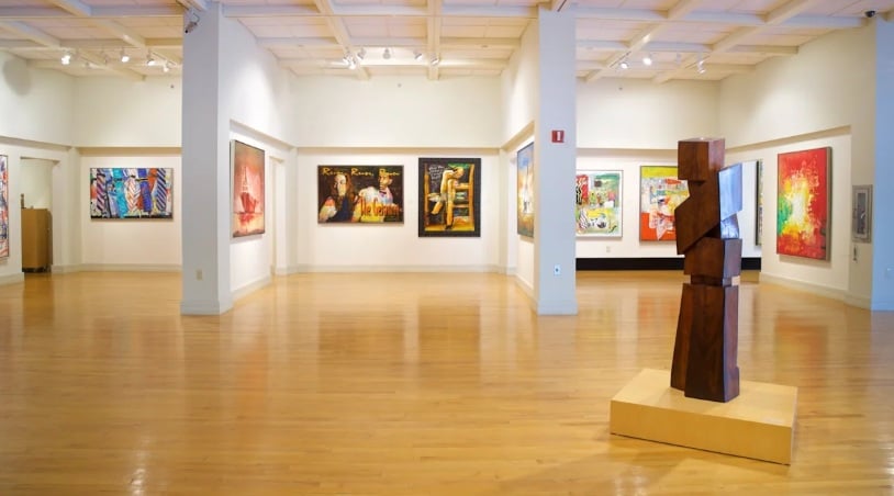 Coral Springs Museum of Art gallery with colorful paintings and a wooden sculpture.