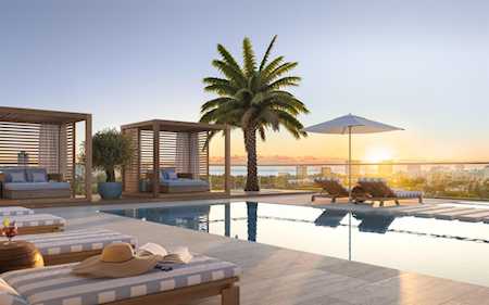 Pool deck with wooden cabanas, lounge chairs, and a palm tree at sunset.