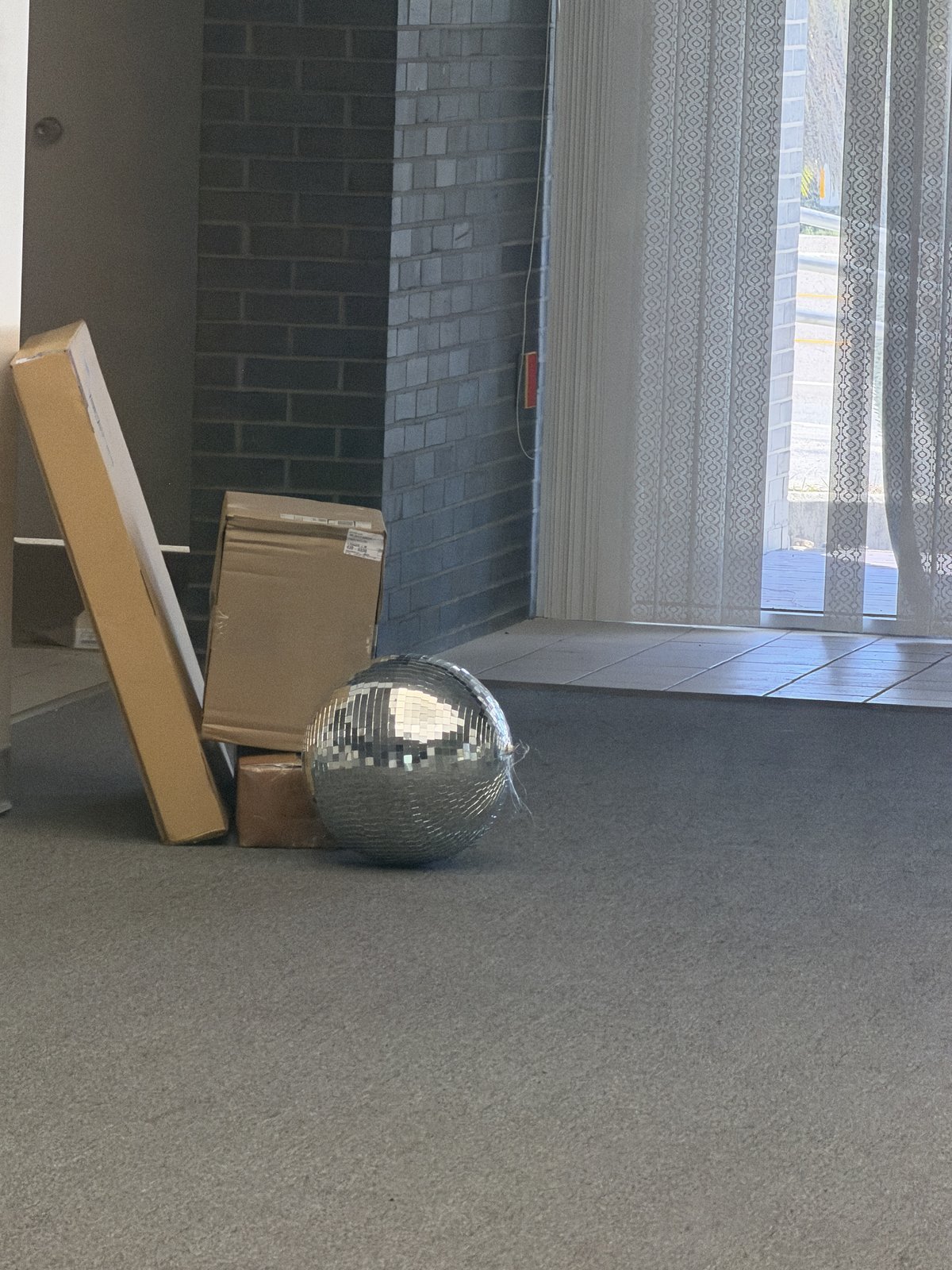 Empty commercial interior with a brick wall, boxes, and a mirrored disco ball beside curtained glass doors.