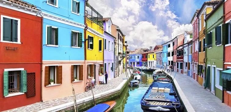 Brightly painted canal-side buildings in red, turquoise, yellow and green, with boats along the water.