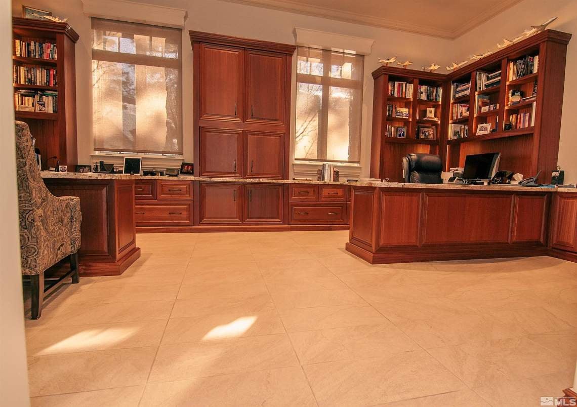 Home office with extensive reddish-brown built-in bookcases and cabinetry, two desks, and a light tile floor.