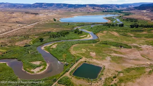 Winding river and wetlands lead toward a lake in a broad valley near Meeker.
