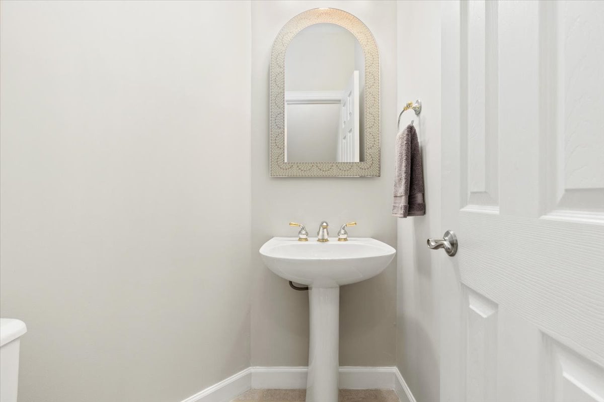 Bathroom with a white pedestal sink, arched mirror, and towel beside the door.