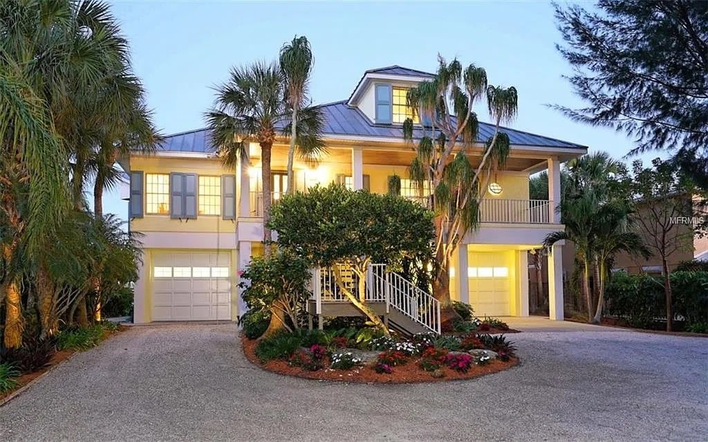 Two-story Florida home with a metal roof, palm trees, and illuminated porches at dusk.