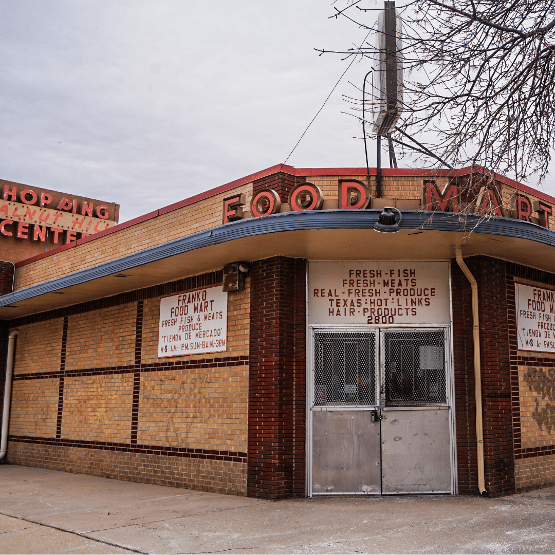 Franko Food Mart storefront at a brick corner building, with a curved blue awning and metal security doors.