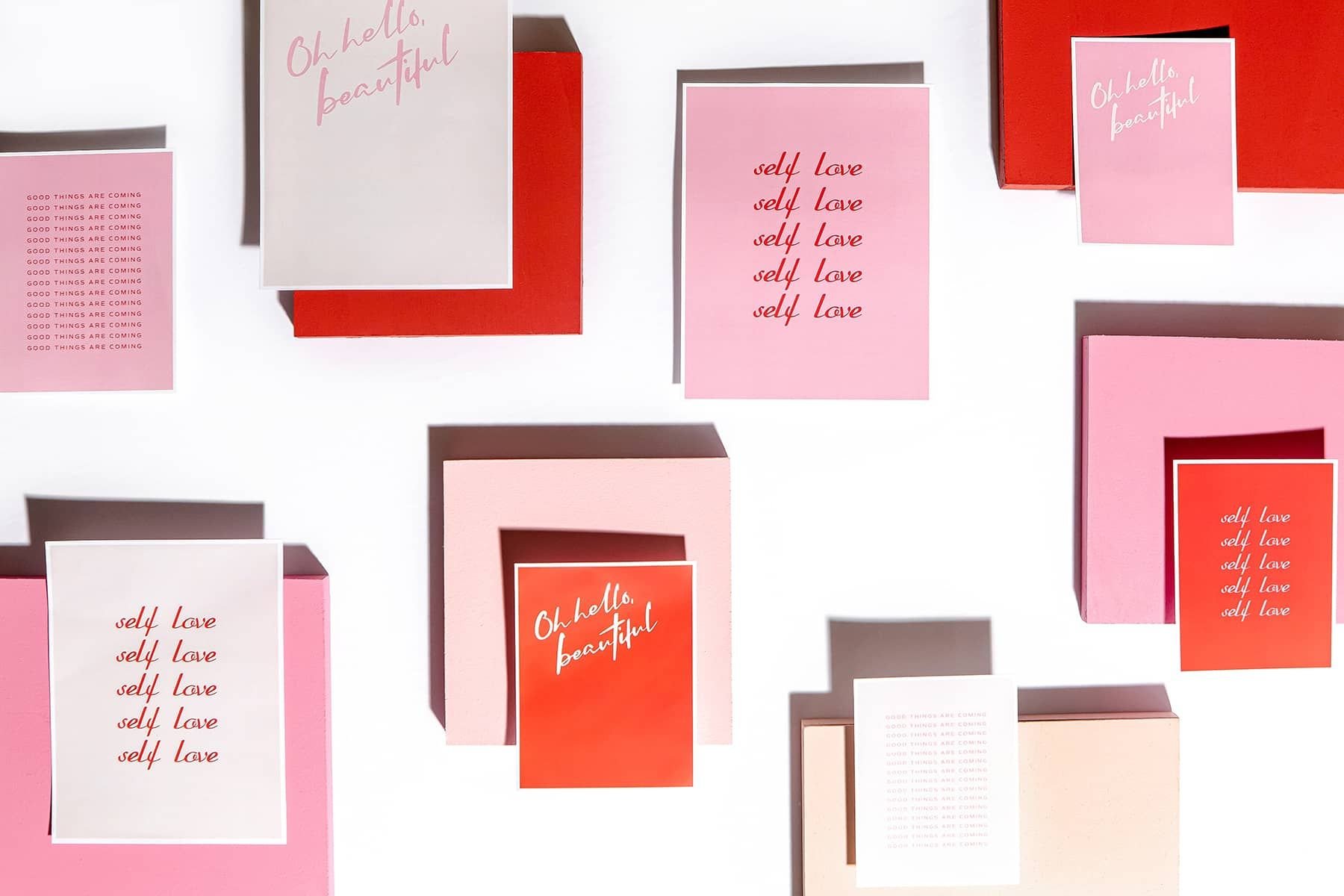 Pink and red Valentine’s Day cards with self-love and encouraging messages arranged among matching boxes.