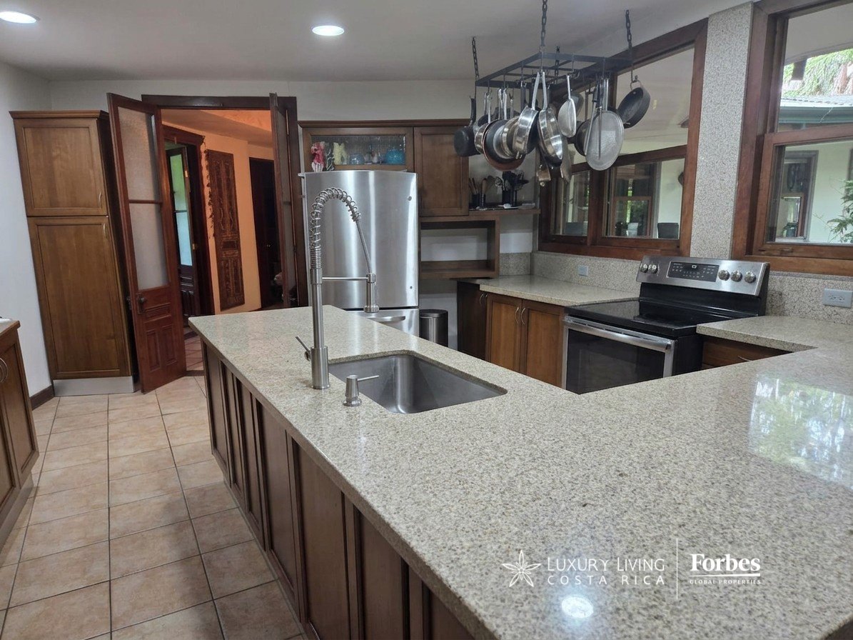 Villa kitchen with a granite island sink, dark wood cabinetry, stainless steel appliances, and hanging cookware.