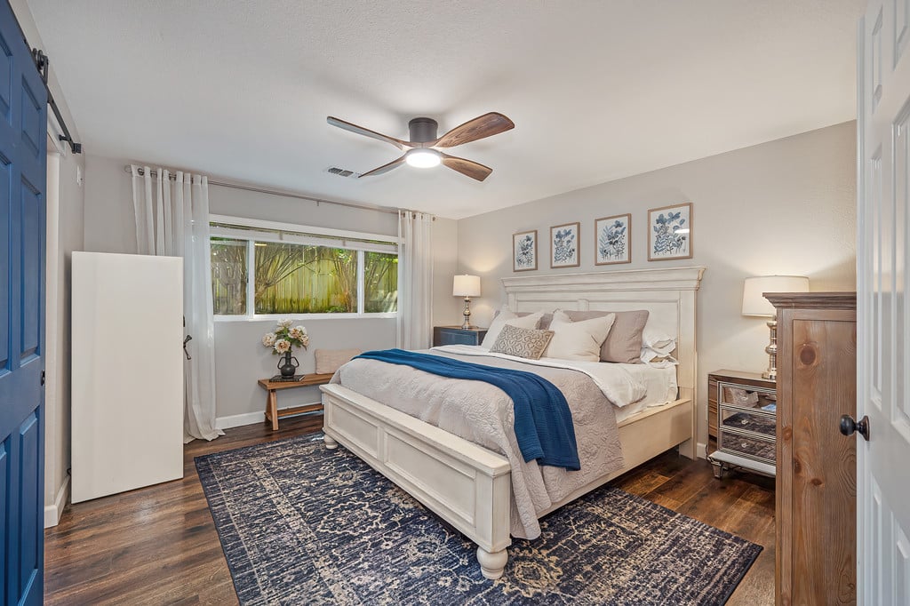Bedroom with a white paneled bed, blue throw, patterned rug, and ceiling fan.