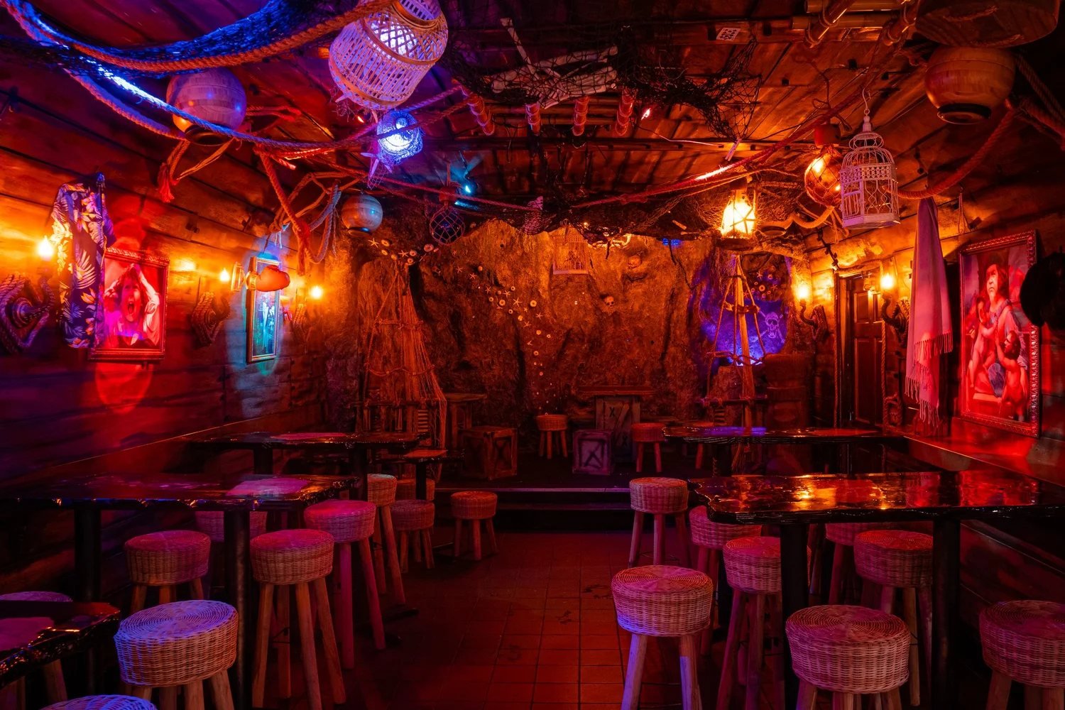 The Lost Inferno's dim interior, lit in red and orange, with rope-wrapped stools and a rocky cave wall.