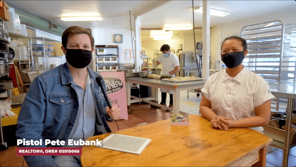 A real estate agent interviews a woman at a wooden table inside Hanloh Thai Food’s kitchen.