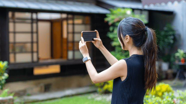 A woman photographs a modern home's glass-fronted entrance from the yard.