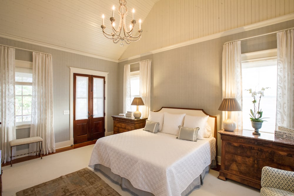 Master bedroom with a white bed, chandelier, French doors, and tall curtained windows.