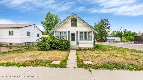 Small gabled house with a covered entry, front walkway, and patchy lawn.