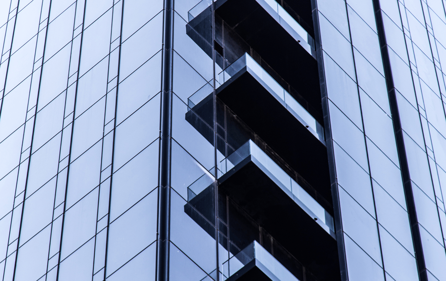 Modern glass high-rise facade with dark balconies projecting between reflective blue panels.