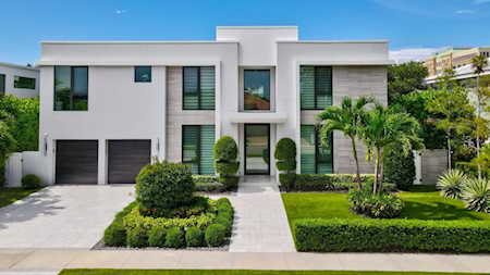 Modern white two-story home with dark-framed windows, two garage doors, and manicured tropical landscaping.