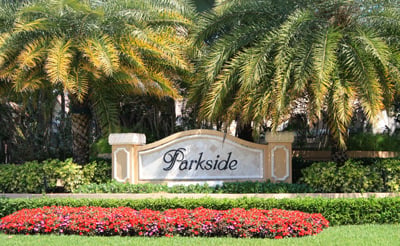 Parkside neighborhood entrance sign framed by palm trees and a bed of red flowers.
