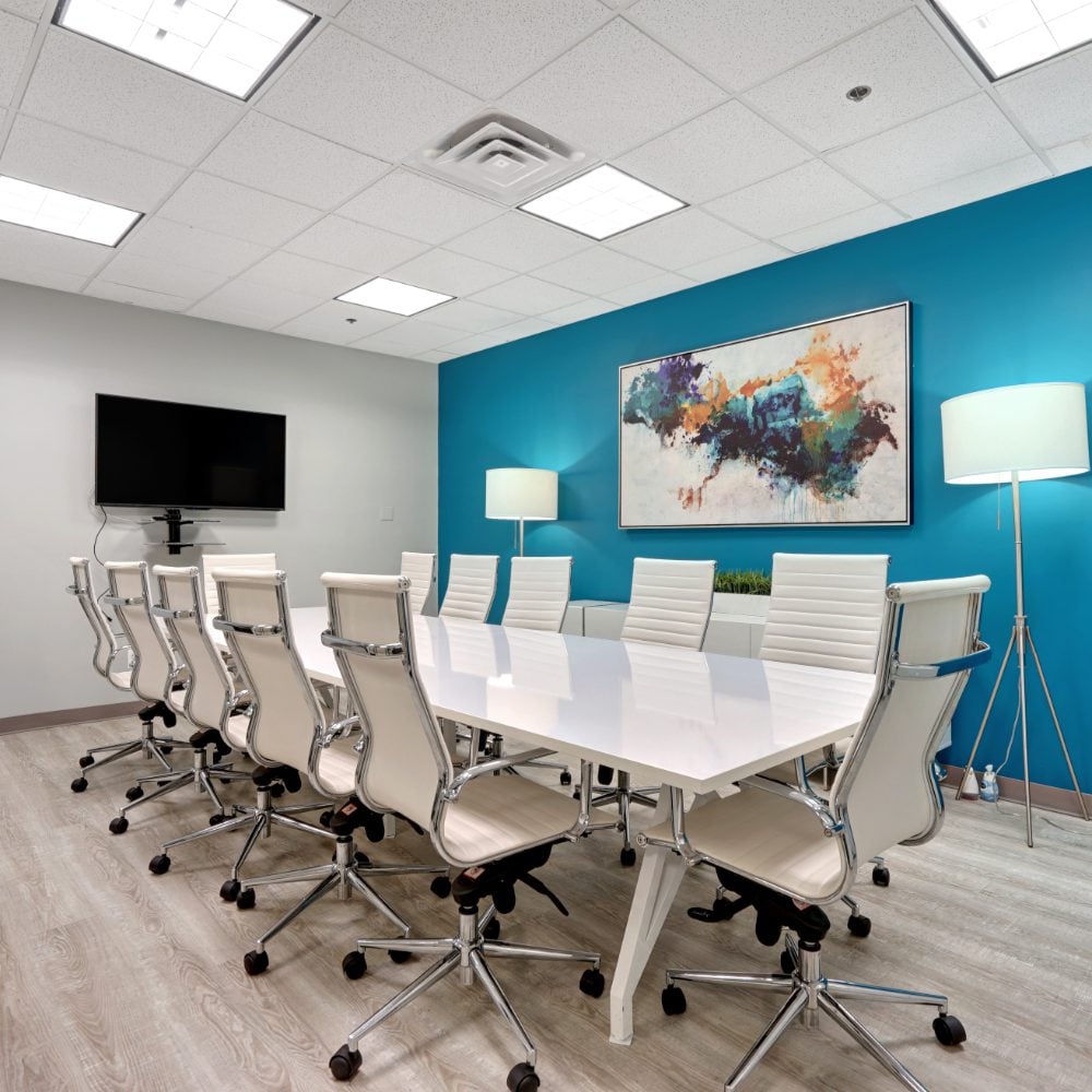Conference room with a long white table, white chairs, and teal accent wall.