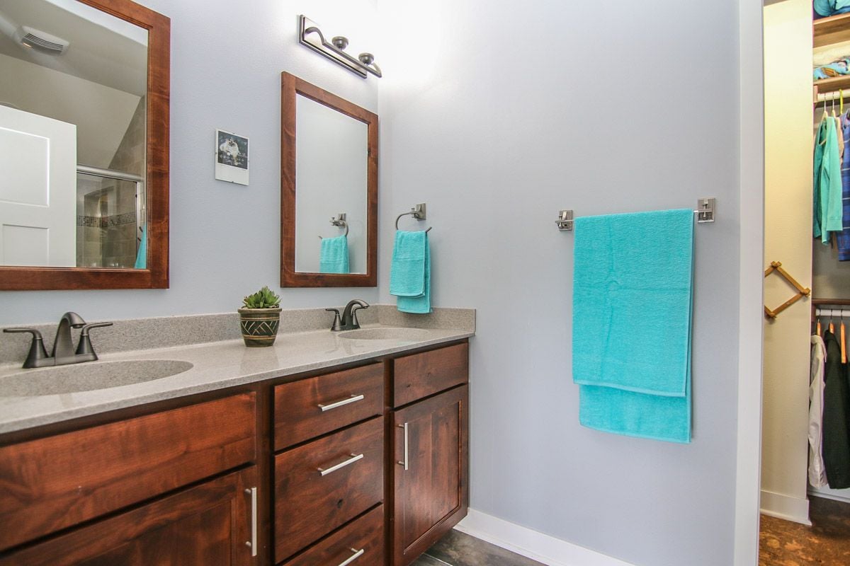 Bathroom with a double-sink wood vanity, turquoise towels, and an open walk-in closet.