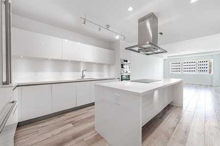 Modern white kitchen with a large island, stainless steel range hood, and wood-look flooring.