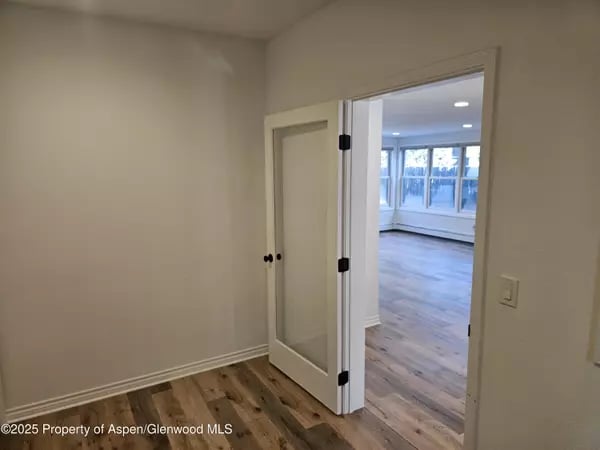 Empty room with wood-look flooring and an open door to a bright room with large windows.