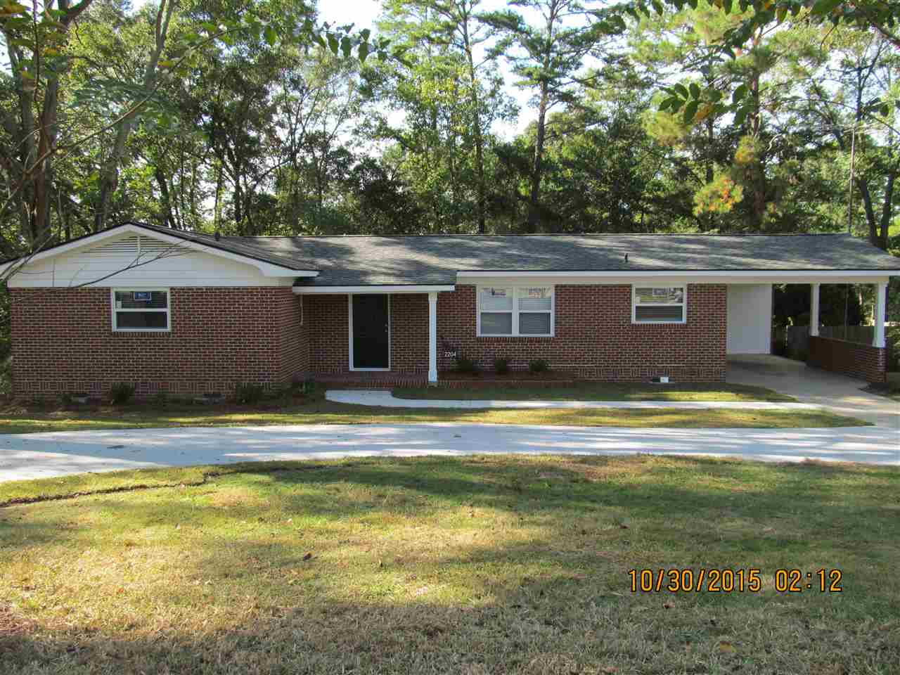 A brick home surrounded by trees, featuring a well-maintained driveway leading to the entrance.