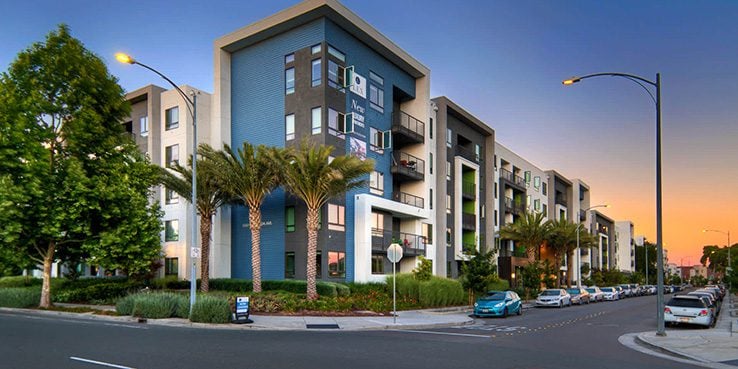 Modern apartment complex with palm trees along a street at sunset.