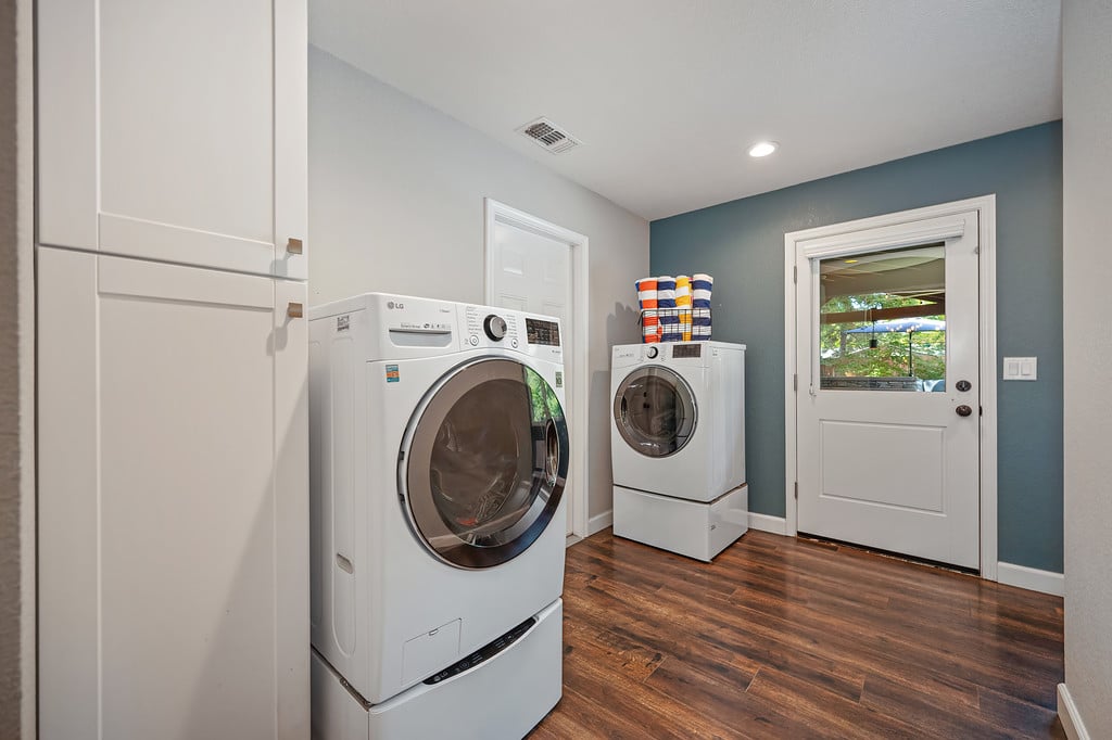Laundry room with white front-loading washer and dryer, tall cabinets, and wood-look flooring.