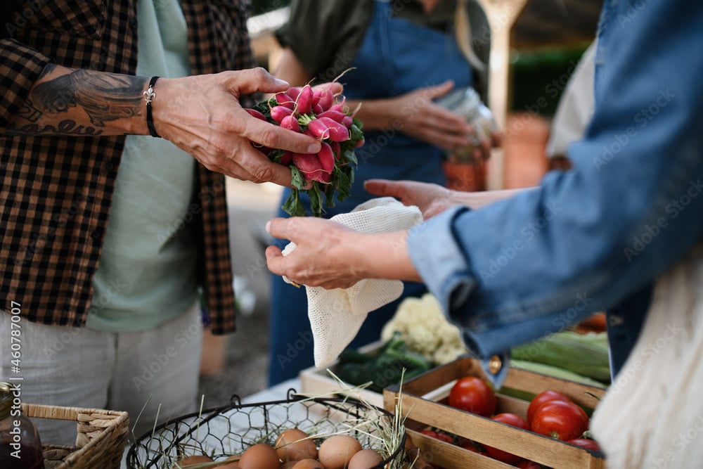 A bundle of red radishes is handed over a market stall with eggs and tomatoes.