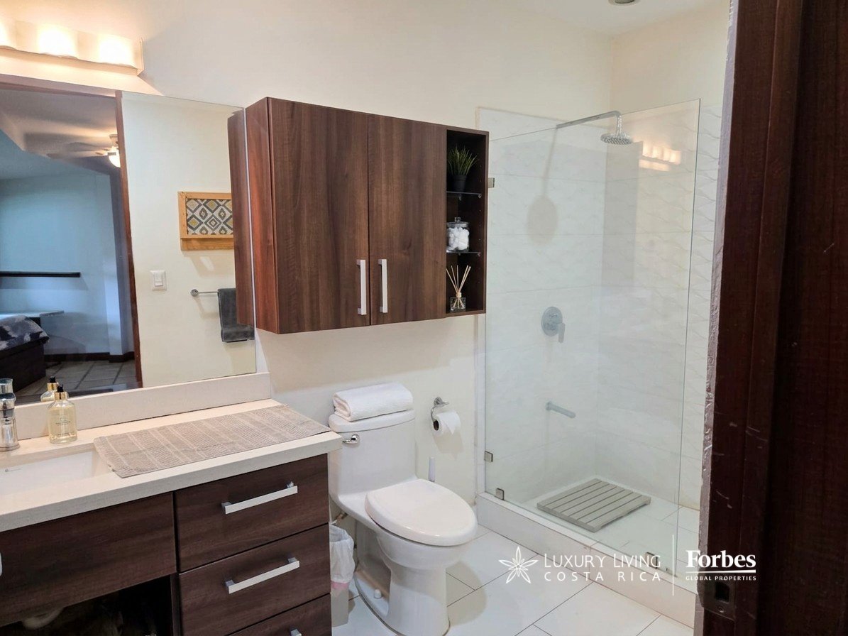 Modern bathroom with dark wood cabinetry, a white vanity, and a glass-enclosed tiled shower.