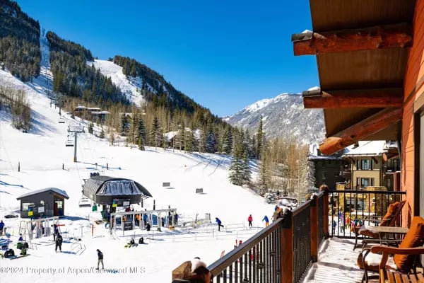 Balcony overlooking a snowy Aspen ski area, with ski lifts and forested mountain slopes.
