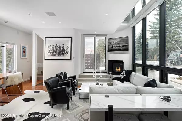 Contemporary living room with a white sectional, black leather chairs, fireplace, and floor-to-ceiling windows.