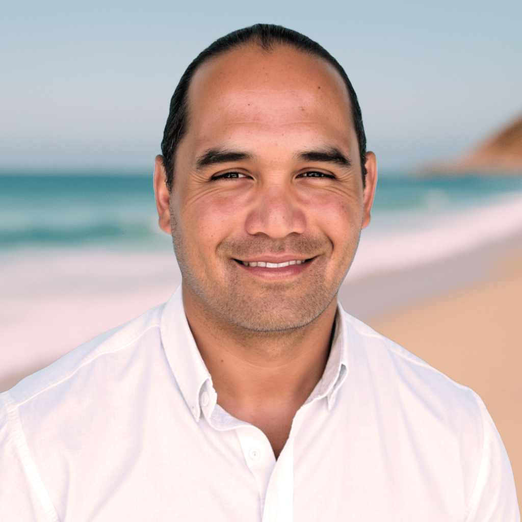 Professional headshot of Gabriel Weisbarth, Realtor at Ocean Element Real Estate in Half Moon Bay, standing in front of a blurred coastal beach backdrop.